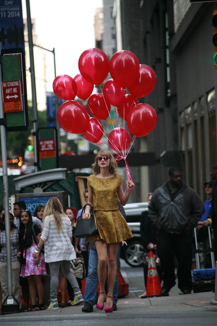 Taylor Swift in gold dress with pink heels holding red balloons