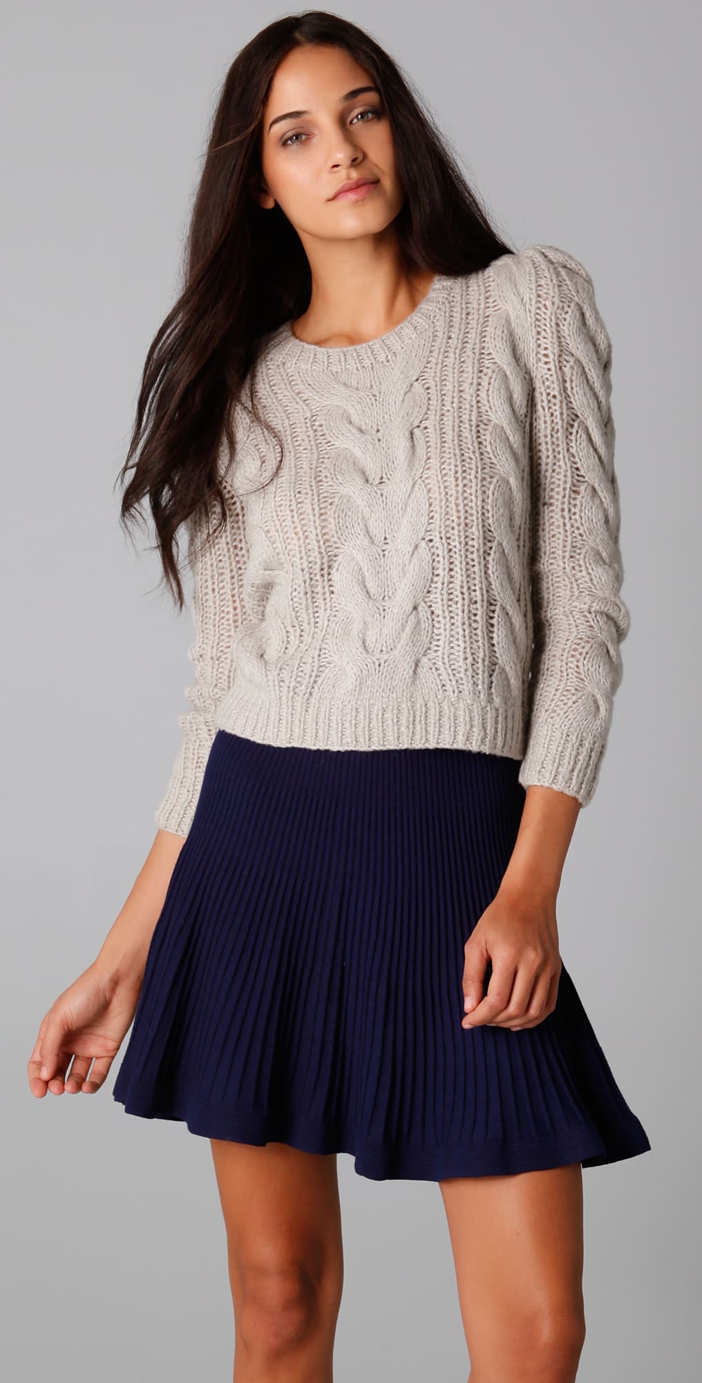 Women's cable knit sweater paired with a mini pleated skirt